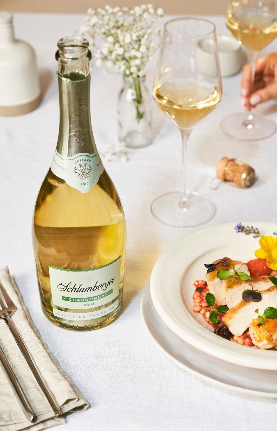 Eine Flasche Chardonnay Reserve steht am gedeckten Tisch neben einem einegschenkten Weihnglas und einem Teller mit mediterranem Hühnchen