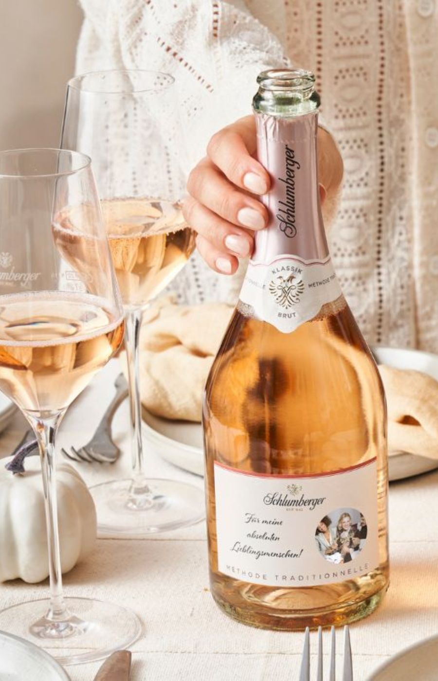 Eine Rose Brut Sektflasche mit personalisiertem Etikett seht auf einem gedeckten Tisch mit gefüllten Gläsern