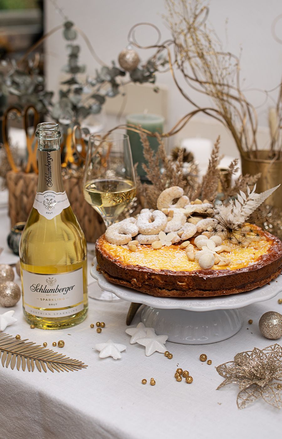 Schlumberger Sparkling steht auf einem weihnachtlich gedeckten Tisch neben einem Cheesecake mit Vanillekipferl