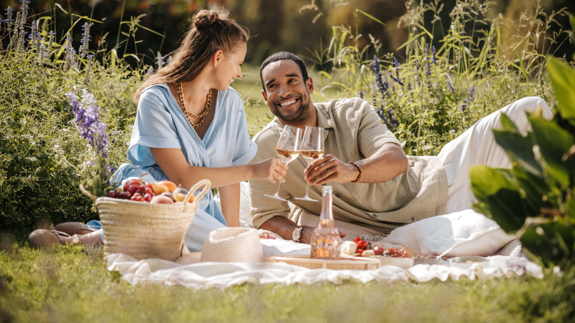 Zwei Personen sitzen im im Park auf der Picknickdecke und trinken Rosé Sekt