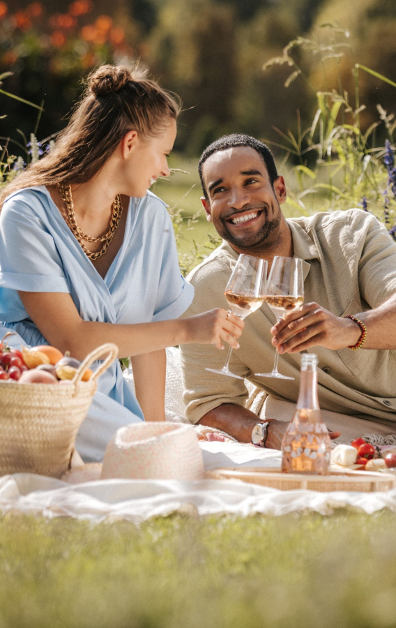 Zwei Personen sitzen im im Park auf der Picknickdecke und trinken Rosé Sekt
