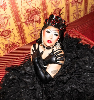 Drag Queen sitzt auf einem roten Sofa mit schwarzem Kleid