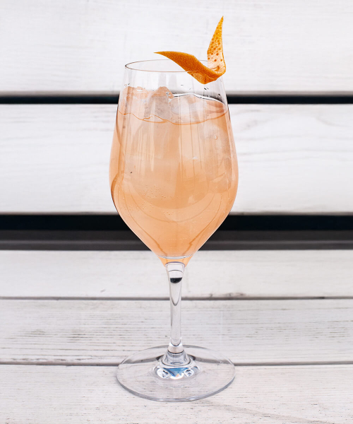 Ein Weinglas gefüllt mit einem Smoky Paloma Cocktail und am Rand eine Orangenzeste, auf einer weißen Bank