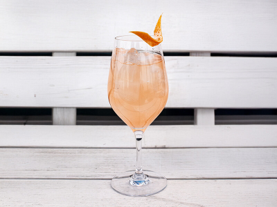 Ein Weinglas gefüllt mit einem Smoky Paloma Cocktail und am Rand eine Orangenzeste, auf einer weißen Bank