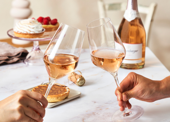 Zwei Personen stoßen mit Weingläsern gefüllt mit Rosé Sekt an