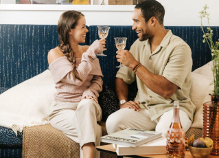 Ein Paar sitzt auf einer Couch und stoßt mit zwei Gläsern Rose an