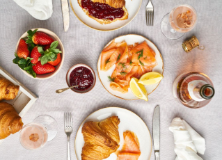 Sekt, Croissants, Erdbeern und Lachs stehen auf einem gedeckten Frühstückstisch