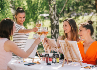 Vier junge Damen sitzen im Garten, trinken Rosé Sekt und malen ein Bild