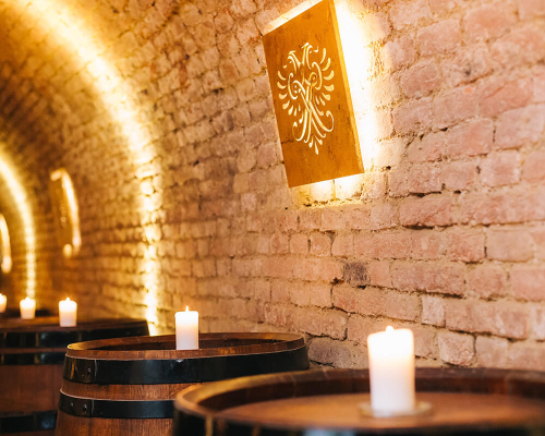 Ein stimmungsvoll beleuchtete Sektkeller mit Fässern und Kerzen darauf.