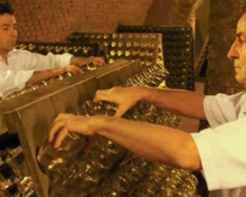 Zwei Männer stehen an einem traditionellen Rüttelpult und schütteln Sektflaschen.